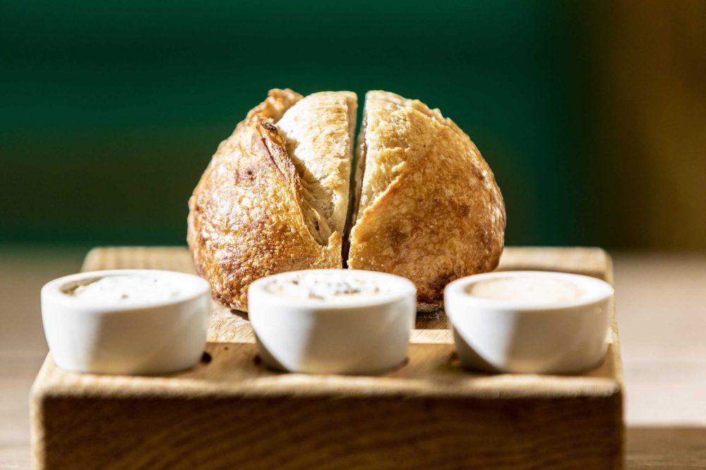 Delicious Italian bread bowl with crispy crust served with three dipping sauces on a wooden tray. Perfect for authentic Italian dining experiences at FiFi's Italian.