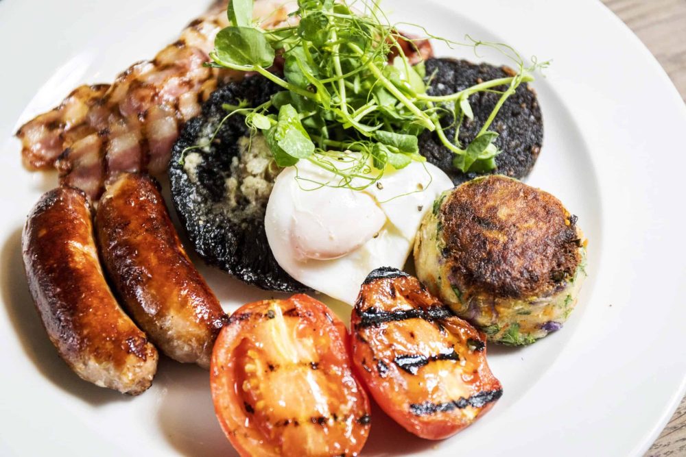 Sausages, grilled tomatoes, and roasted vegetables on a white plate at FiFi's Italian restaurant.